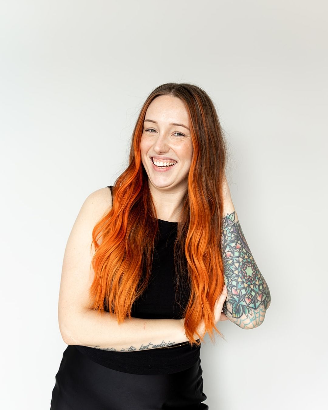 Woman with vibrant orange hair and tattoos on a plain background
