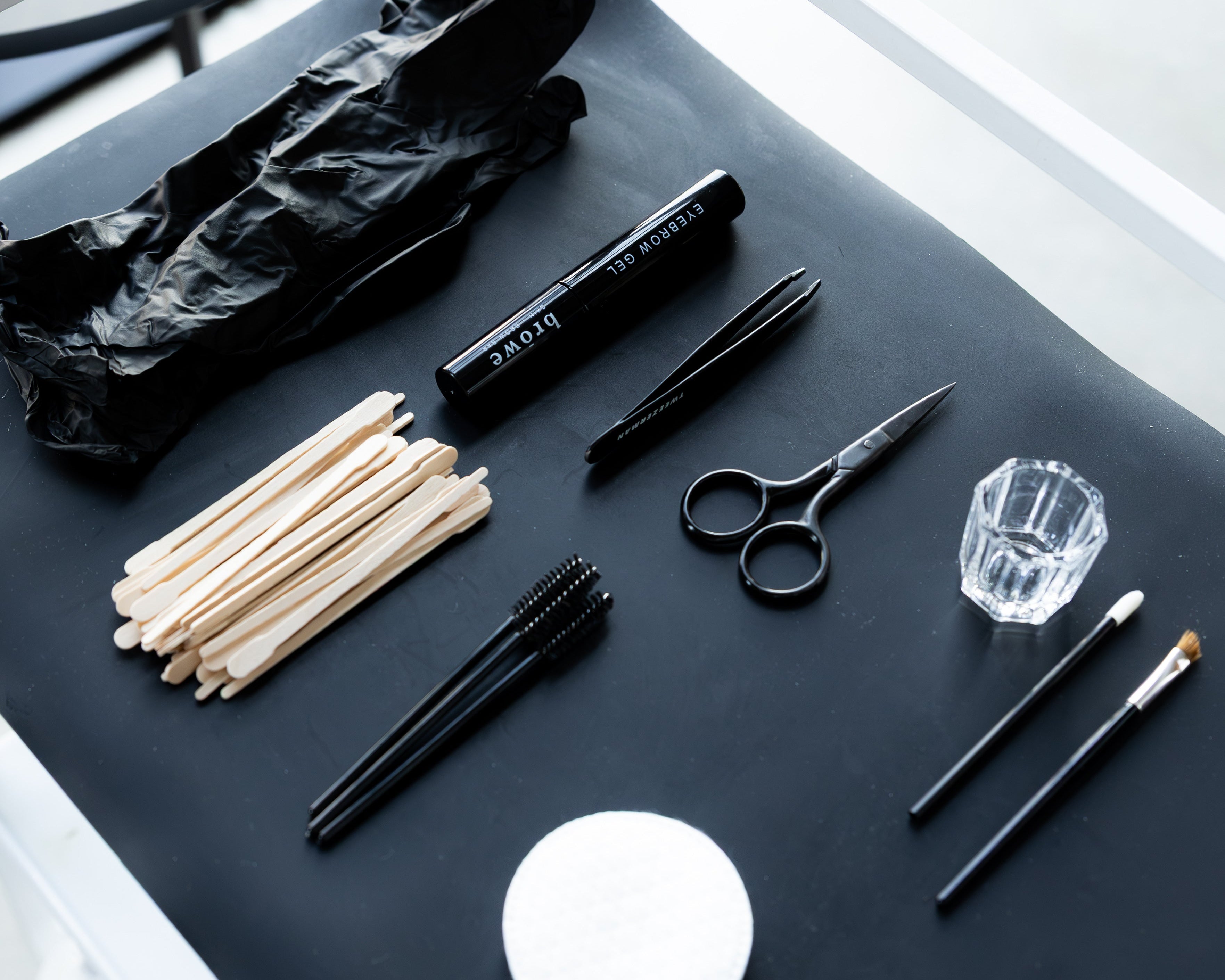 Collection of makeup and grooming tools on a dark surface with a white chair in the background.
