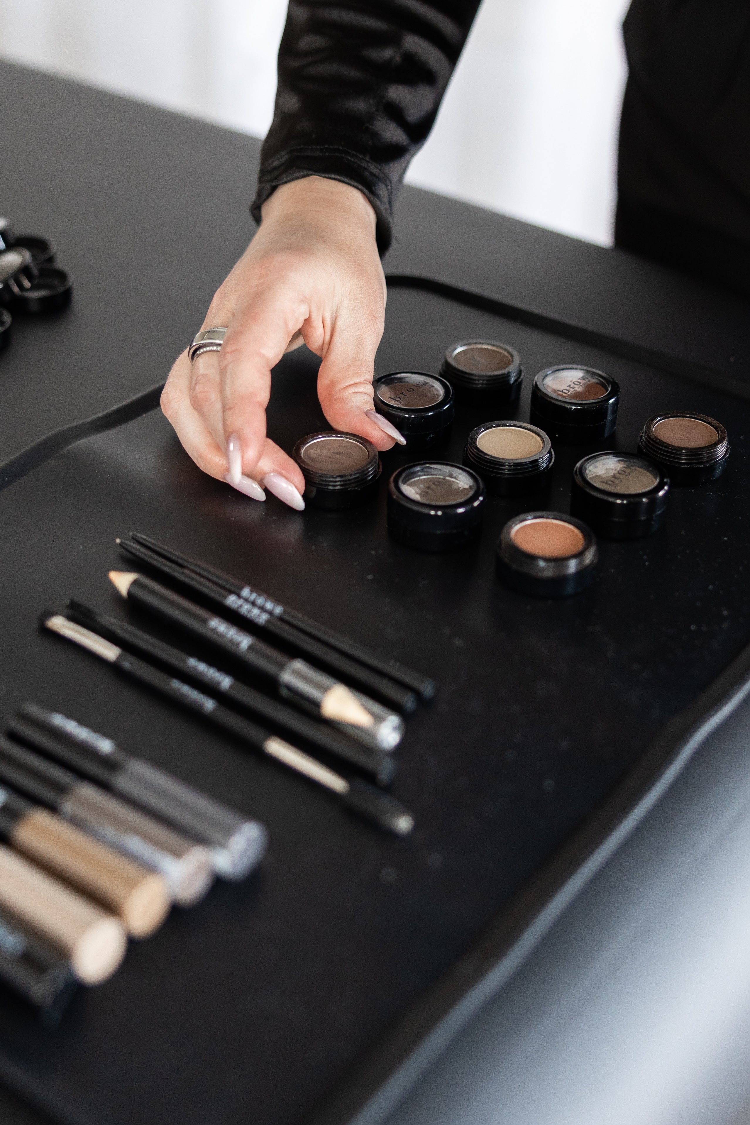 Makeup brushes and compact powders on a black tray with a hand reaching for a compact powder.