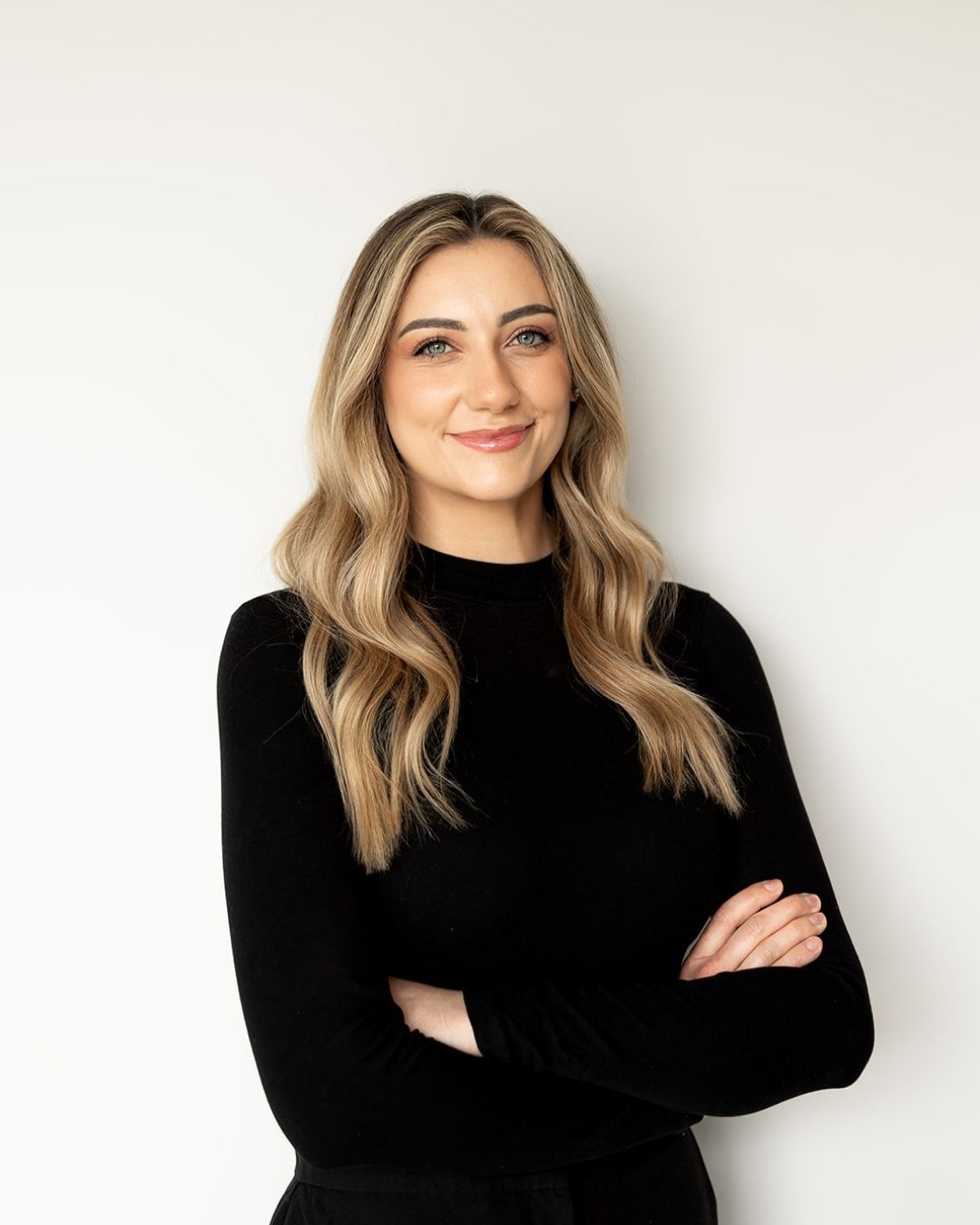Woman with long blonde hair wearing a black sweater against a white background