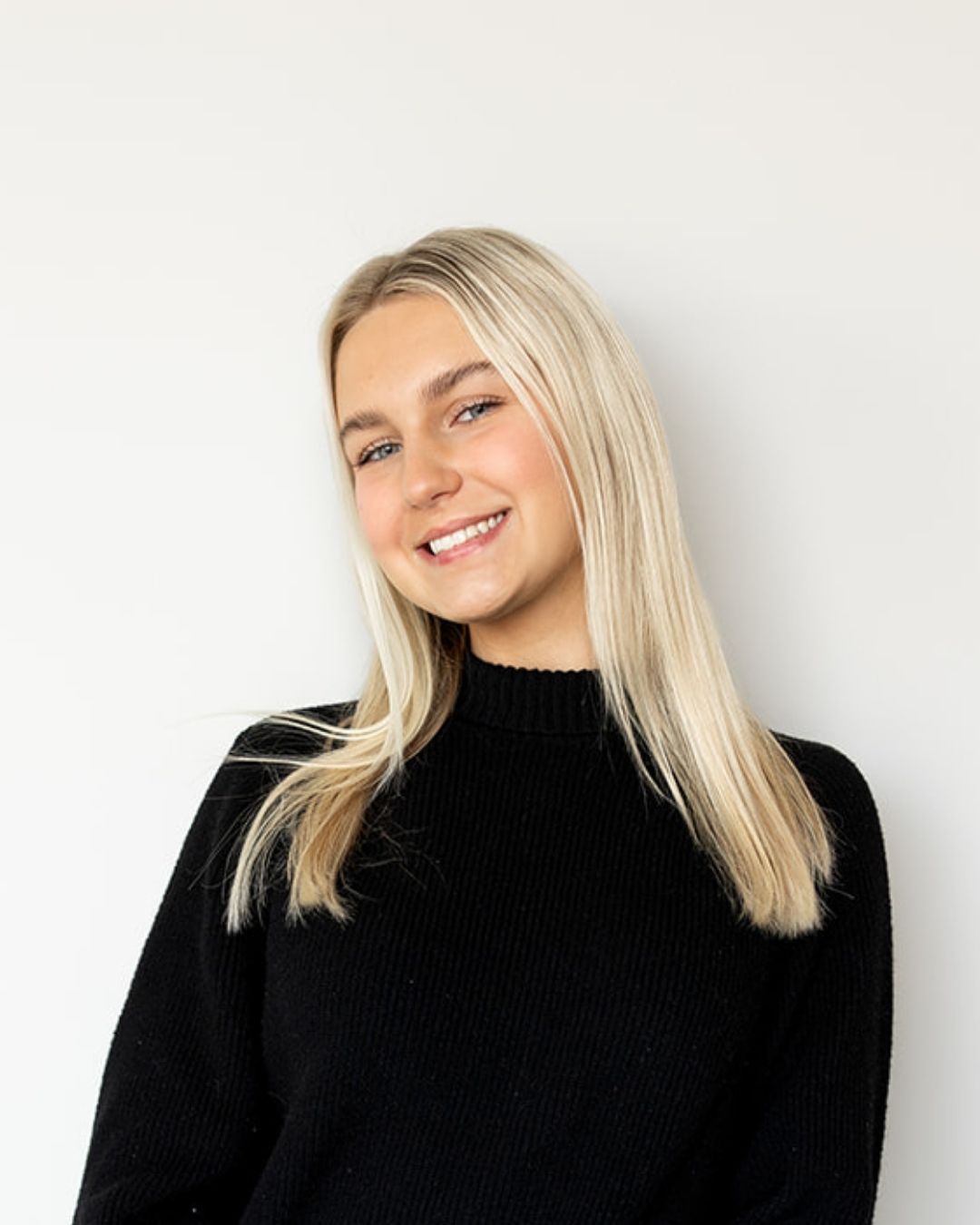 Woman with blonde hair wearing a black sweater against a white background