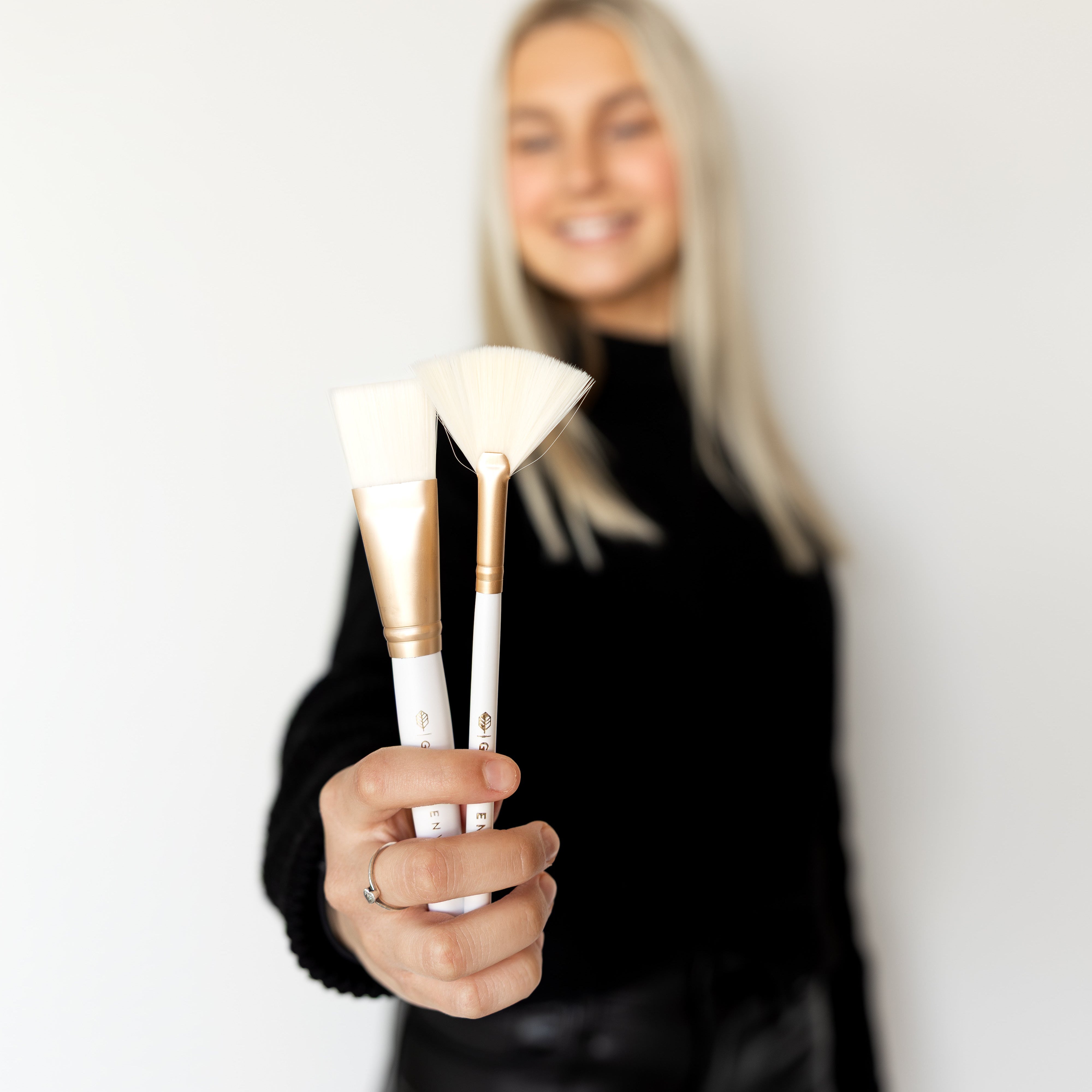 Person holding makeup brushes with a plain background