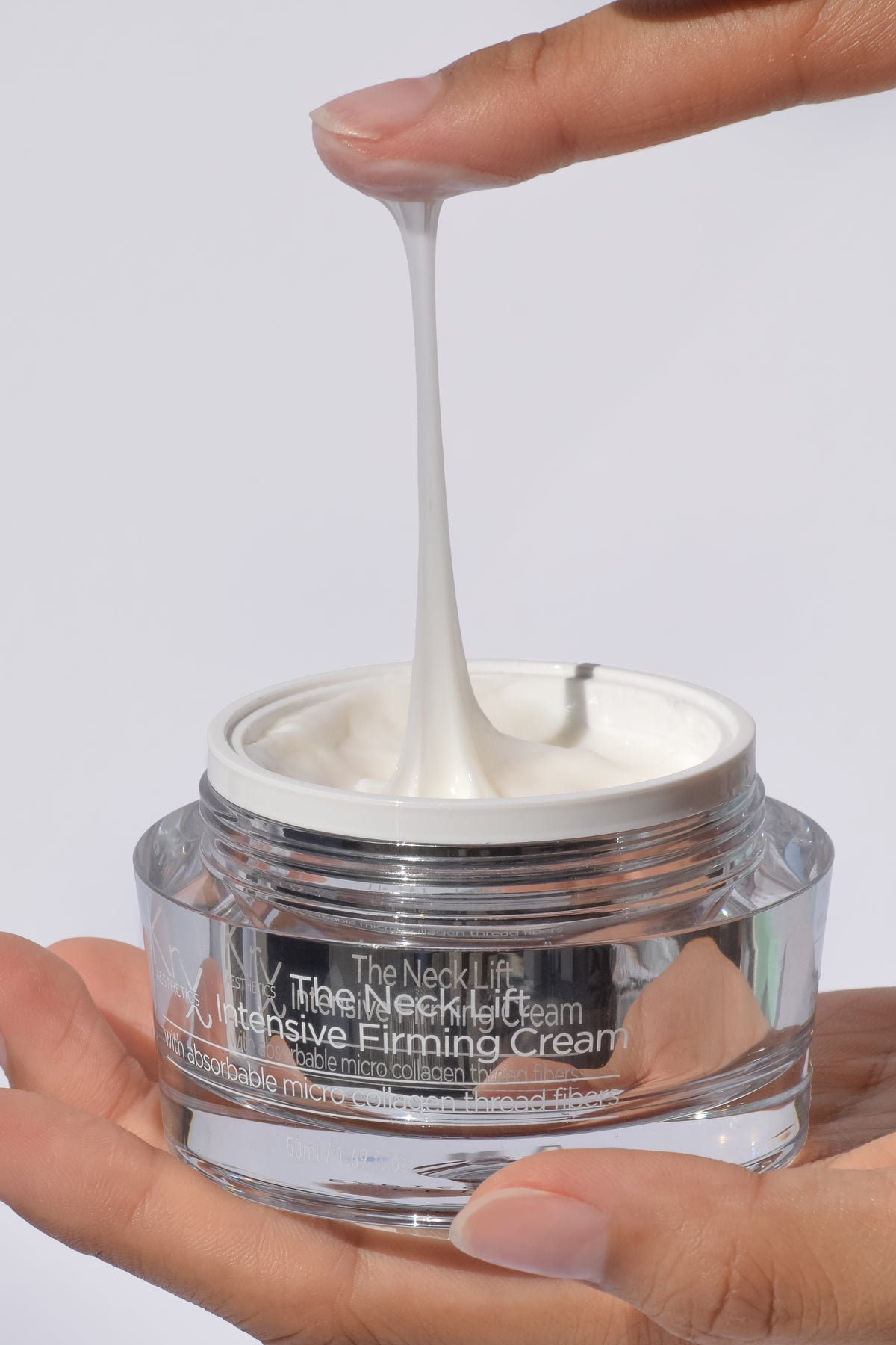 Hand holding a jar of intensive firming cream with cream being squeezed out.