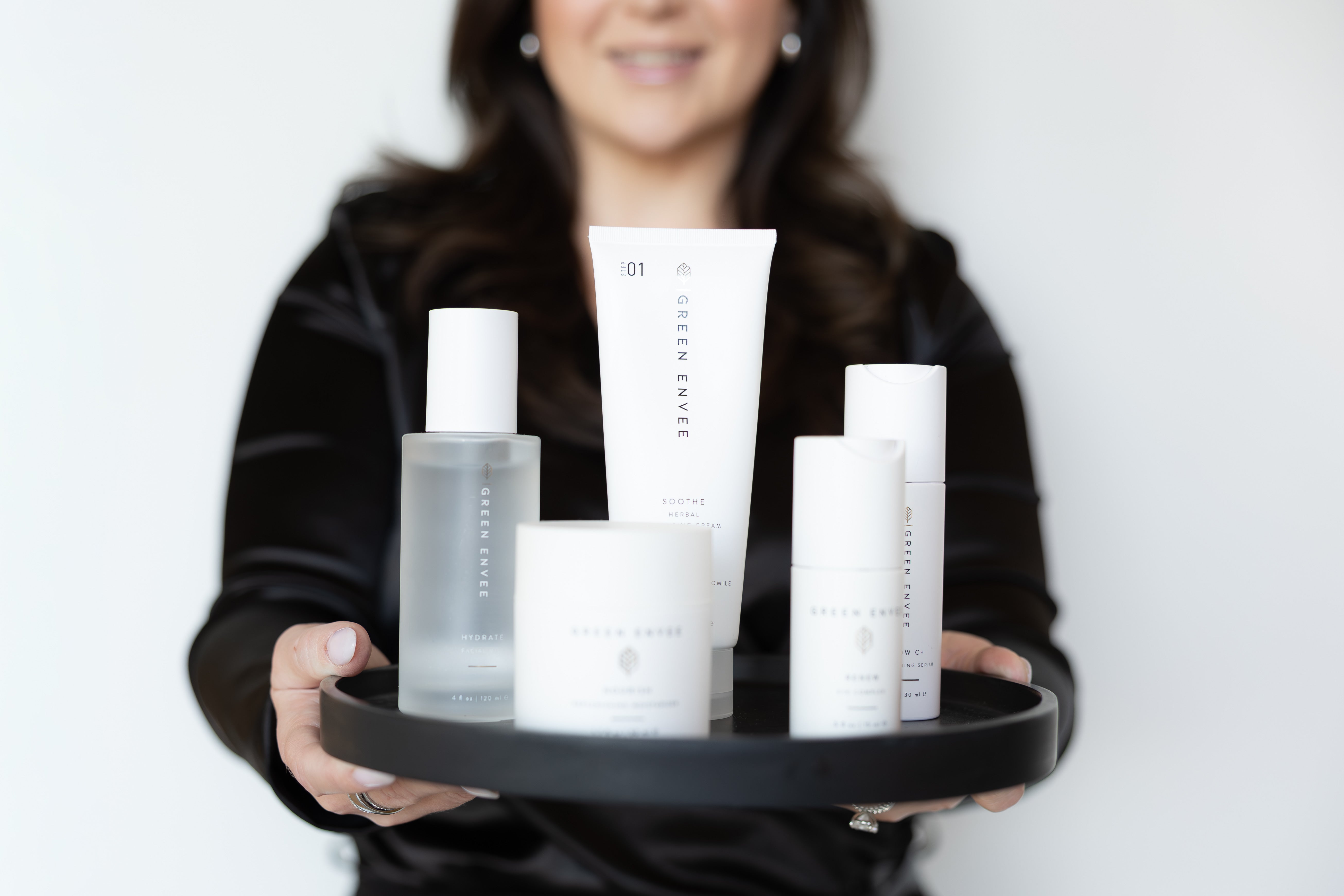 Person holding a tray with skincare products against a white background